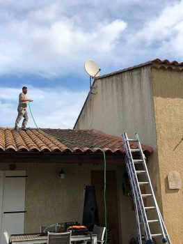 Homme sur un toit en tuile nettoyant une façade sale à Istres.